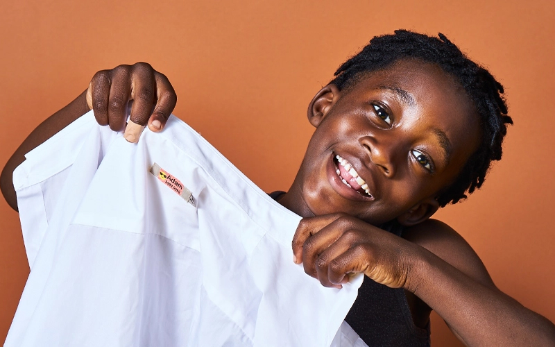 Jonge jongen die een shirt vasthoudt met het opstrijklabel van My Nmatags erop, op een oranje achtergrond